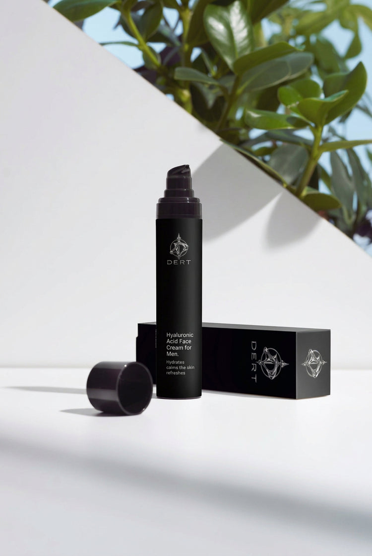 A black cylindrical pump bottle labeled 'Oil-Free Dry Skin Gel for Men' stands next to its matching black box and detached cap on a white surface. The background features a diagonal white panel with green leaves and blue sky visible in the upper right, overlaid with repeated 'selfnamed' watermarks.